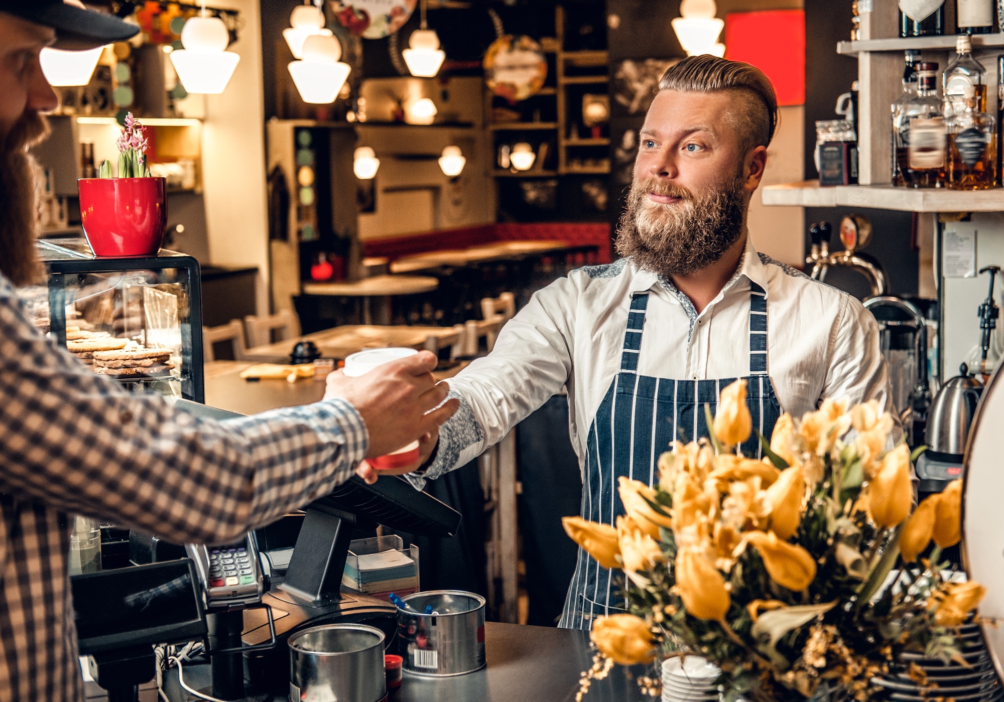 A man selling coffee to a consumer in a coffee shop.