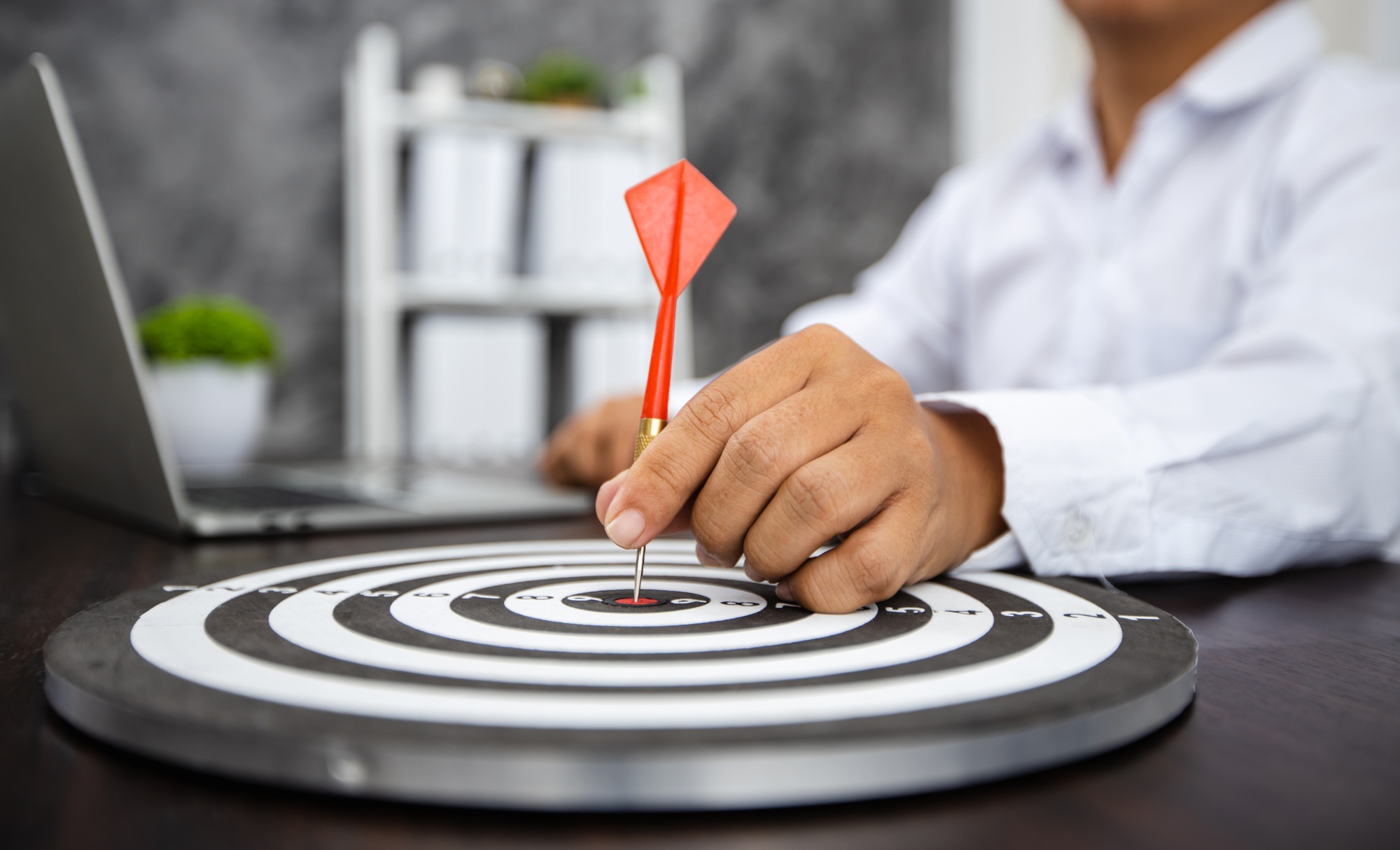 Close up hand of business man holding dart on target with financial graph paper with laptop on table