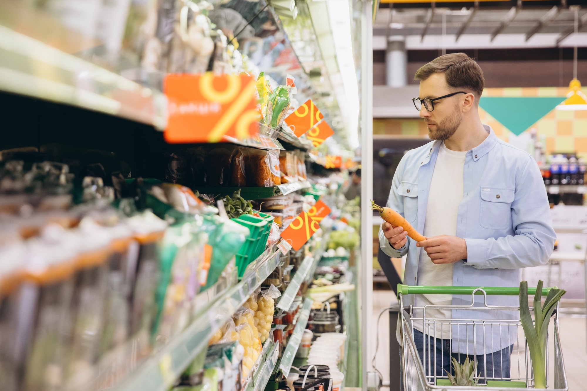 Customer choosing groceries in a supermarket, holding a carrot and looking at the discount prices