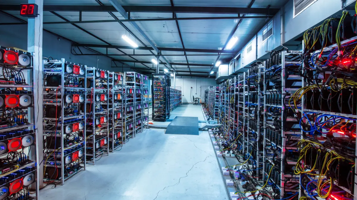 Long rows of cryptocurrency mining rigs with cables and red fans on metal shelves in a large warehouse