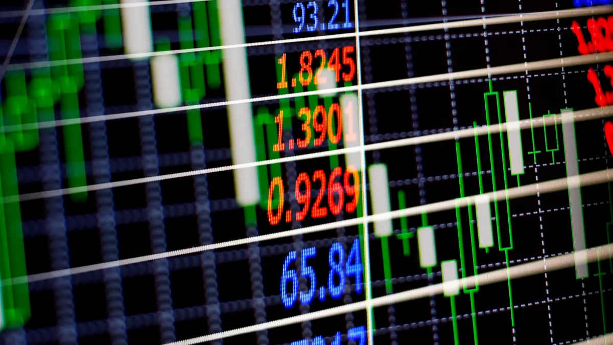 Close-up of an electronic stock exchange board with candlestick charts and red, orange and blue price numbers
