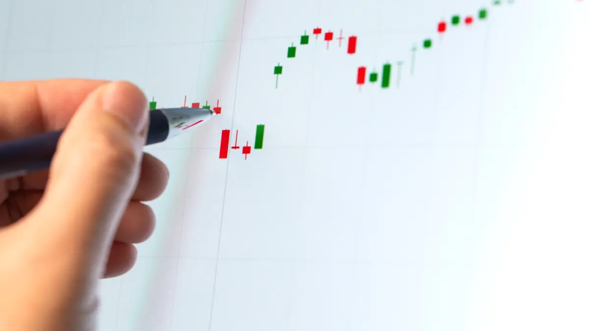 Hand holding a pen pointing at a red and green candlestick chart on a white screen