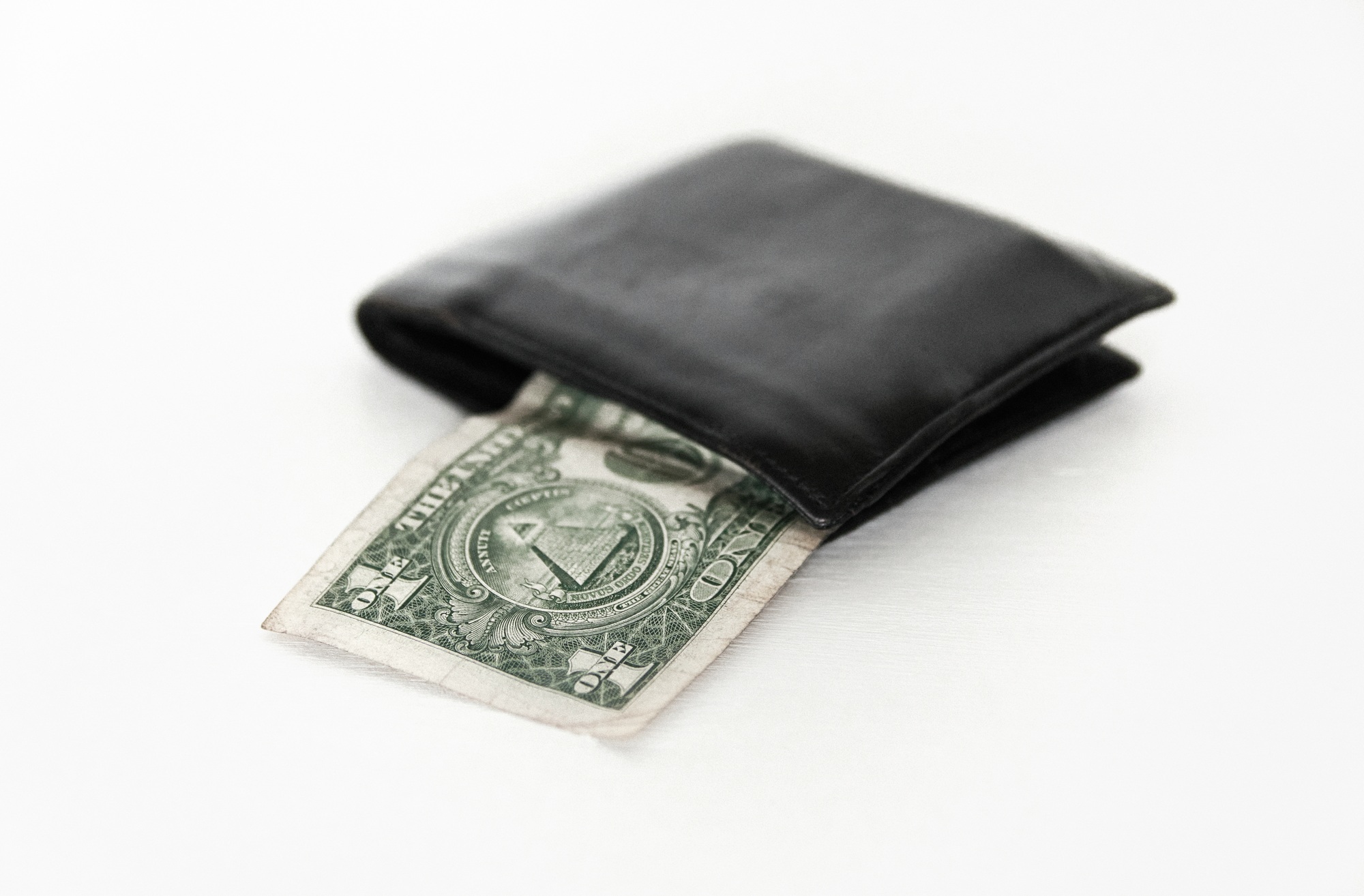 Close-up image of black wallet and dollar bill on white background.