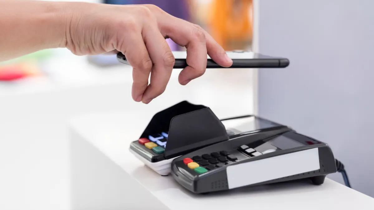 Hand holding a smartphone over a card payment terminal to make a contactless mobile payment