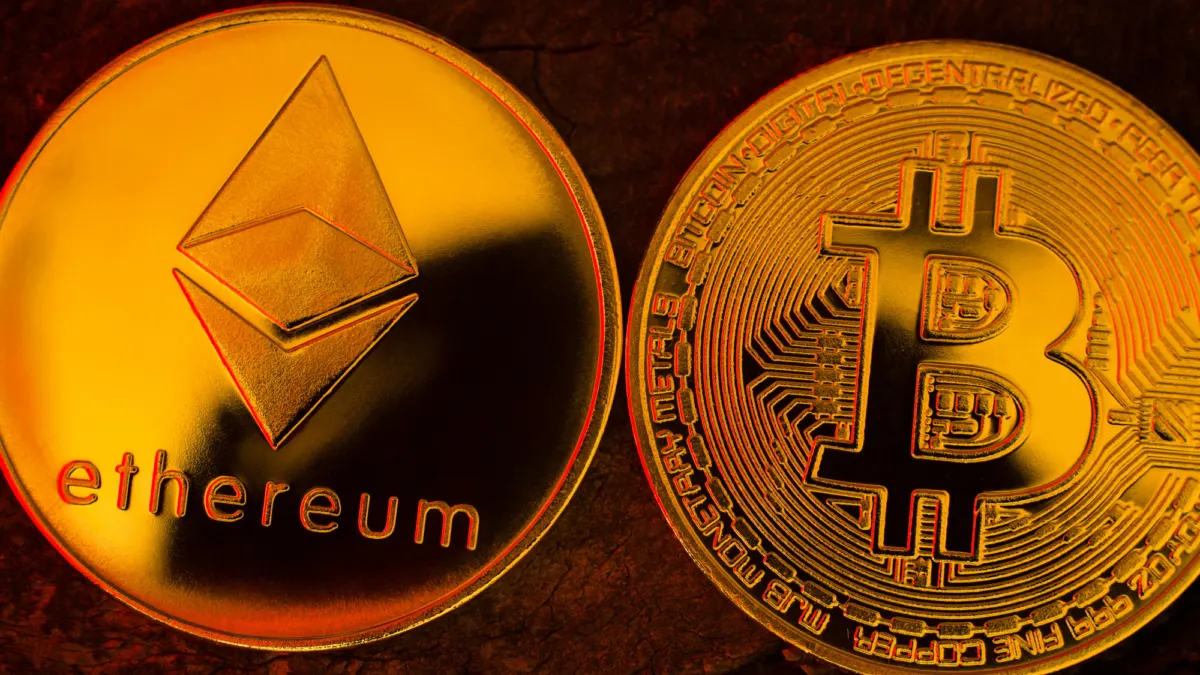 Two gold-colored coins, one with the Ethereum logo and one with the bitcoin symbol, side by side on dark wood