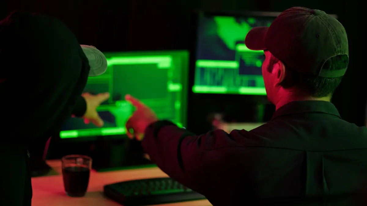 Two people in a dark room looking at computer screens with green code, illustrating crypto theft and hacking