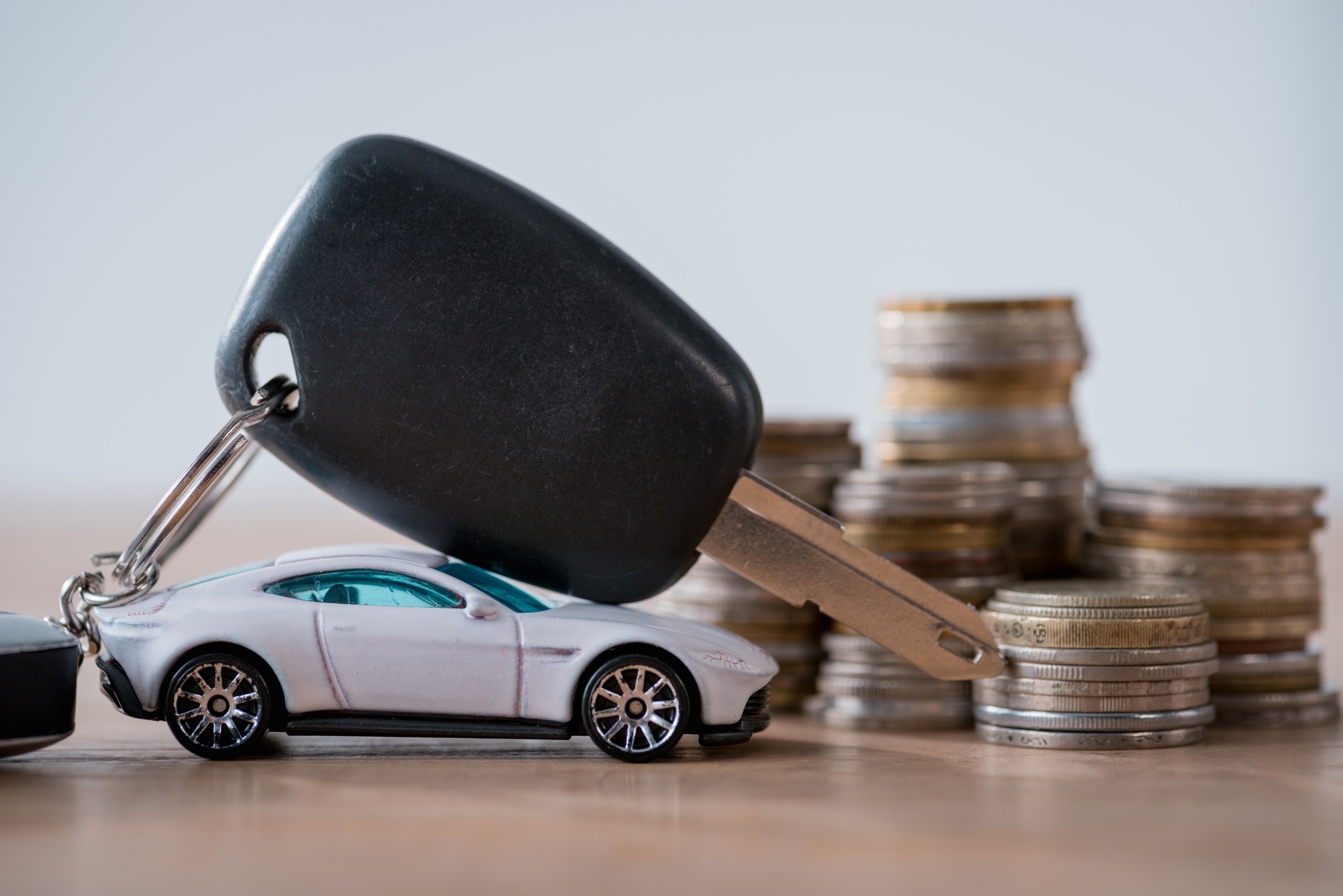 miniature car, car keys and metal coins on wooden surface isolated on grey