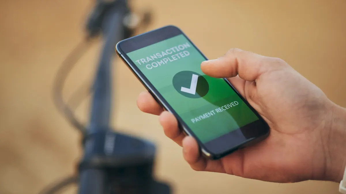Hand holding a smartphone showing a transaction completed, payment received screen in a banking app