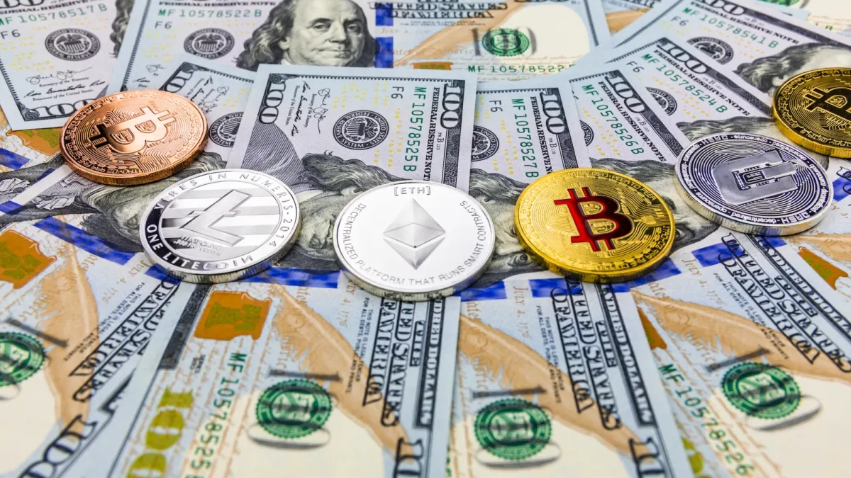 Bitcoin and other cryptocurrency coins resting on a spread of US one hundred dollar banknotes